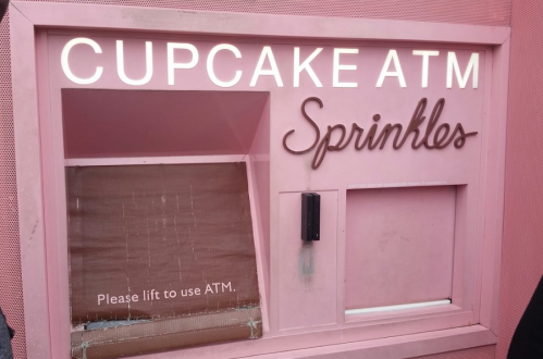 A pink cupcake ATM with the words "Cupcake ATM" and "Sprinkles" illuminated above a slot for dispensing cupcakes.