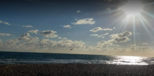 A serene beach scene with gentle waves, fluffy clouds, and a bright sun shining over the water.