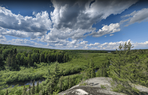 A panoramic view of a lush green landscape with a winding river under a cloudy blue sky.