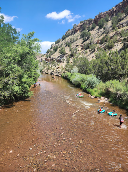 A scenic river flows through a rocky landscape, with people enjoying the water on colorful floats under a blue sky.