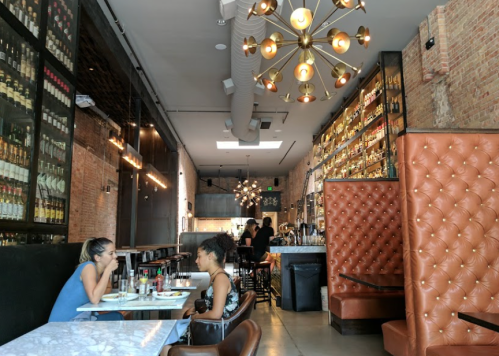 A modern restaurant interior with a bar, two diners at a table, and stylish lighting fixtures.