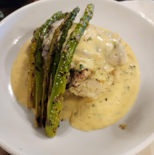 A plate featuring grilled asparagus and a piece of fish topped with creamy sauce, served over a bed of mashed potatoes.