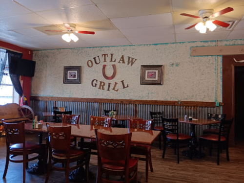Interior of Outlaw Grill featuring wooden tables, chairs, and a rustic decor with a horseshoe emblem on the wall.