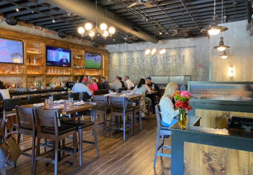 Interior of a modern tavern with a bar, tables, and patrons enjoying their meals. TVs display sports in the background.