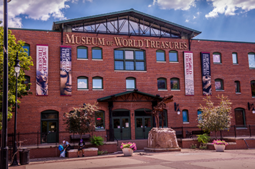 Exterior of the Museum of World Treasures, featuring brick architecture and banners, with a sculpture in front.