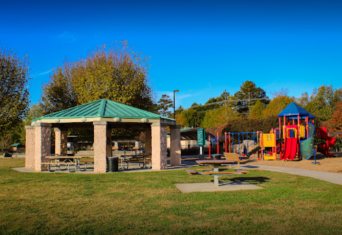 A park scene featuring a picnic pavilion and a colorful playground with slides and climbing structures.