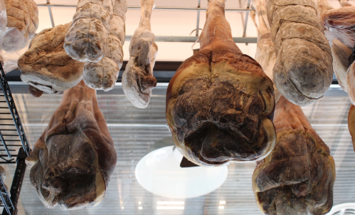 Hanging cured meats displayed on a rack, showcasing various shapes and textures.