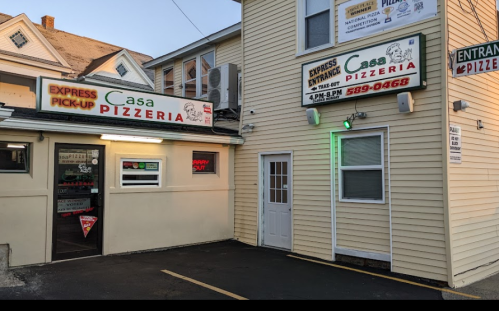 Exterior of Casa Pizzeria, featuring signs for express pick-up and entrance, with a parking area visible.
