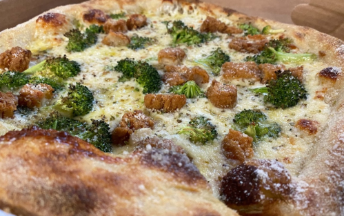 A close-up of a pizza topped with broccoli and golden-brown pieces, featuring a crispy crust and melted cheese.