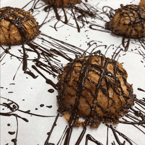 Coconut macaroons drizzled with chocolate on parchment paper, showcasing a delicious dessert presentation.