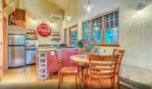 Cozy kitchen with a round dining table, wooden chairs, and a Coca-Cola sign, featuring modern appliances and warm lighting.