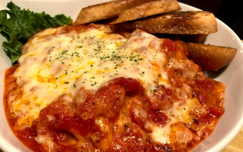 A bowl of cheesy pasta with marinara sauce, garnished with herbs, served with toasted bread on the side.