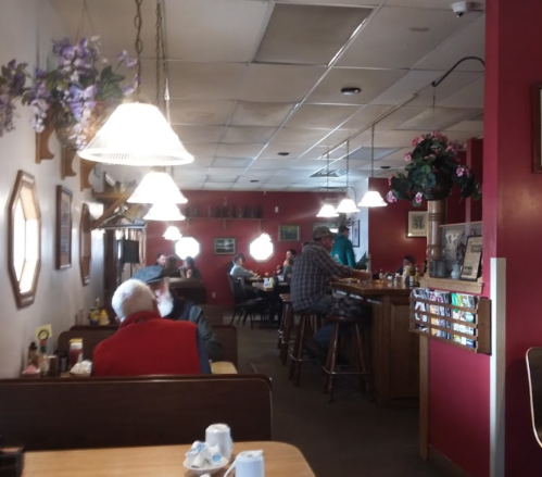 A cozy diner interior with red walls, tables, and patrons enjoying their meals. Soft lighting from hanging lamps.