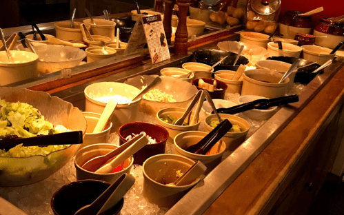 A buffet station with various bowls of ingredients, including salads and sauces, arranged on ice.