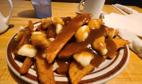 A plate of sweet potato fries topped with cheese curds and drizzled with brown gravy.