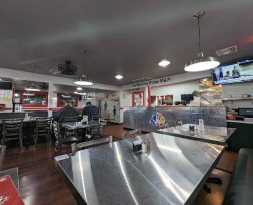 Interior of a casual restaurant with metal tables, chairs, and a TV, featuring a mural and a welcoming atmosphere.