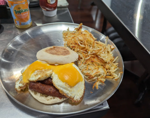 A plate with a breakfast sandwich featuring eggs, sausage, and cheese, alongside crispy hash browns.