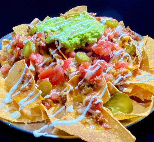 A plate of nachos topped with guacamole, diced tomatoes, jalapeños, and drizzled with sour cream.