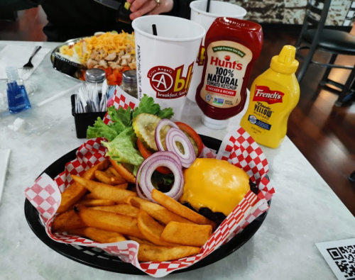 A plate of fries and a cheeseburger with lettuce, tomato, onion, and condiments on a table in a casual dining setting.