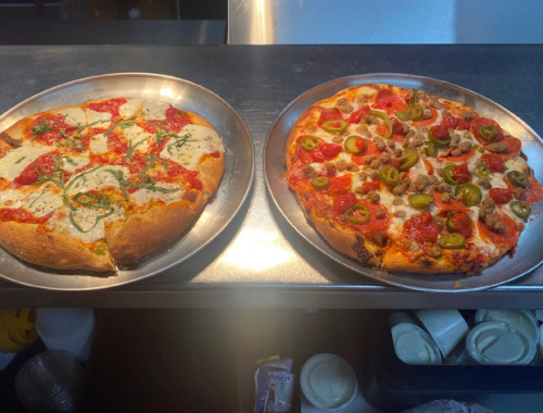 Two pizzas on metal trays: one with white sauce and herbs, the other topped with red sauce, pepperoni, and jalapeños.