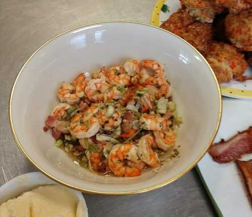 A bowl of shrimp mixed with vegetables and seasoning, served alongside a plate of crab cakes and mashed potatoes.