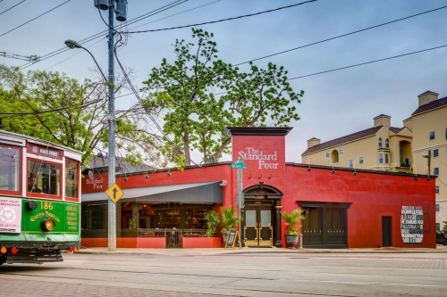 A vibrant red building with "The Standard Pour" sign, featuring a streetcar in front and trees nearby.