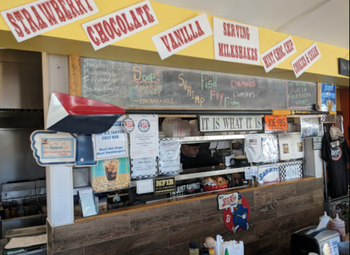 A colorful diner counter with a menu board, serving milkshakes and various food items, and a staff member behind the counter.