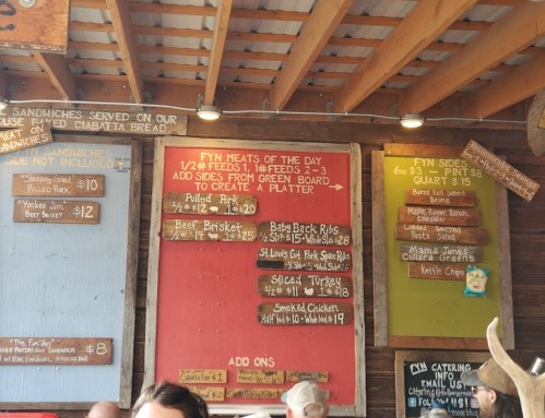 Menu board featuring daily specials and prices for sandwiches, meats, and sides in a rustic setting.