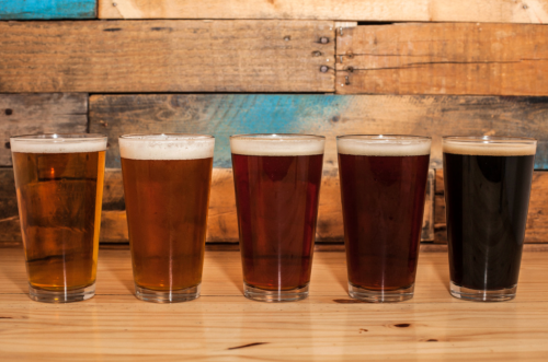 Four glasses of beer in varying shades, lined up against a rustic wooden background.