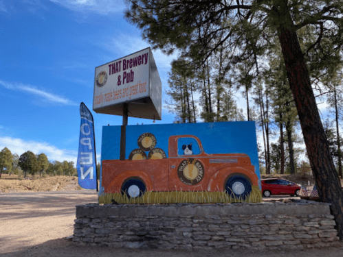 A colorful mural of a vintage truck with barrels, next to a sign for THAT Brewery & Pub in a wooded area.