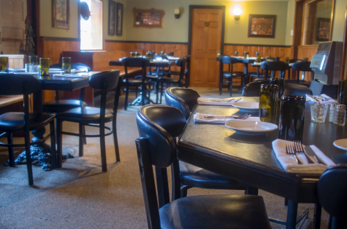 A cozy restaurant interior with empty tables, black chairs, and green accents, creating a warm atmosphere.