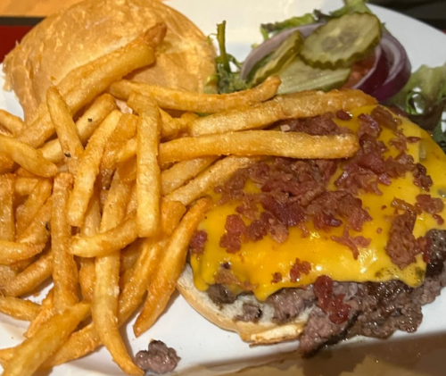 A cheeseburger with bacon on a bun, served with crispy fries and a side salad with pickles and onion.
