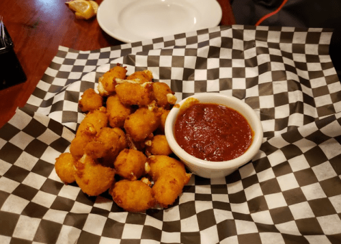 A plate of golden-brown fried snacks served with a small bowl of marinara sauce on a checkered paper.