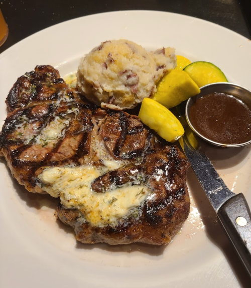 Grilled steak with herb butter, mashed potatoes, and sautéed zucchini and squash on a white plate.