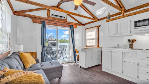Cozy interior of a bright room with a sofa, kitchen, and large windows overlooking a deck and water view.