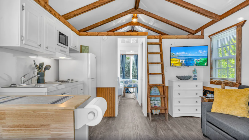 Cozy interior of a small cabin featuring a kitchen, living area, and a lofted sleeping space with wooden beams.