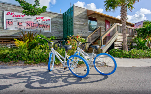 Two bicycles with blue wheels parked in front of a wooden building with a sign for Coconut Cay Resort and Marina.