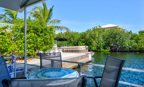 A serene waterfront view with a dock, boat, and lush greenery under a clear blue sky.