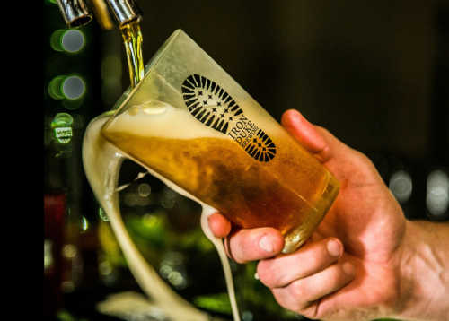 A hand pours beer into a glass with a logo, creating a frothy head as it fills.