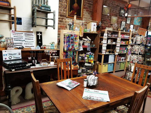A cozy shop interior featuring wooden tables, shelves of colorful products, and decorative items against a brick wall.