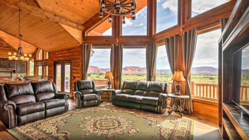 Cozy living room with leather sofas, large windows, and scenic mountain views, featuring wooden beams and a decorative rug.