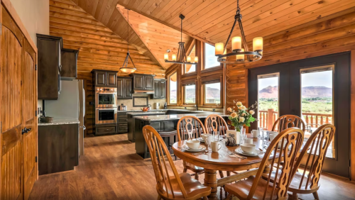 A cozy wooden kitchen and dining area with a large table, modern appliances, and scenic views through large windows.