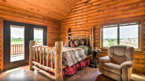 Cozy log cabin bedroom featuring a wooden bed, armchair, and large windows with scenic views.