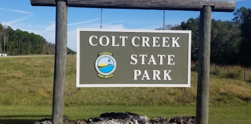 Sign for Colt Creek State Park in Florida, featuring the park's logo and surrounded by greenery.