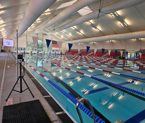 Indoor swimming pool with lanes, starting blocks, and flags, featuring a large screen and American flag in the background.