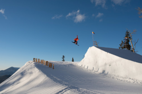 A snowboarder jumps off a snowy ramp with a clear blue sky in the background, showcasing a winter sports scene.