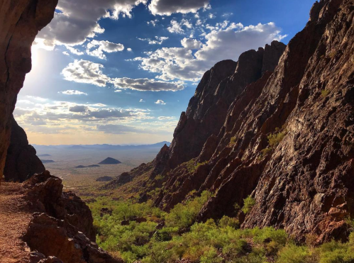 A scenic view of rocky cliffs and a vast desert landscape under a bright blue sky with scattered clouds.
