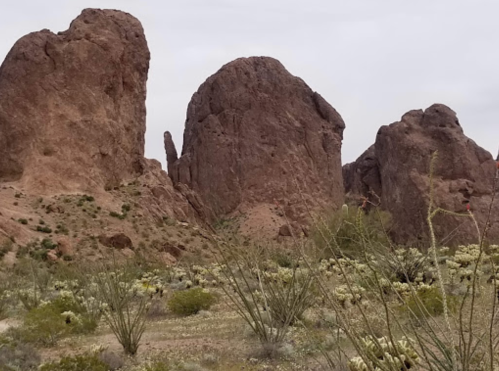 Rock formations rise above a desert landscape, surrounded by sparse vegetation and a cloudy sky.