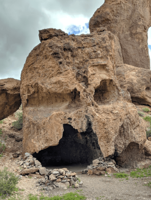 A large rock formation resembling a skull, surrounded by smaller stones and greenery under a cloudy sky.