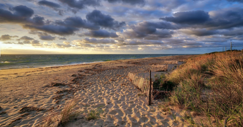A serene beach at sunset, with sandy shores, gentle waves, and a cloudy sky.